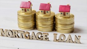 Conceptual footage of MORTGAGE LOAN words with golden coins and tiny model houses.