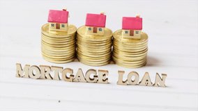 Conceptual clips of MORTGAGE LOAN words with miniature model houses and golden coins