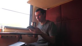 man is sitting on the train Railway carriage holding a smartphone and drinking lifestyle coffee and tea. slow motion video. man writes messages in the smartphone in the train social media. man with