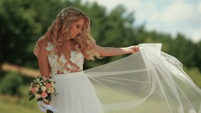 A beautiful young bride with a bouquet is spinning in anticipation of the groom on the street. Wedding day.