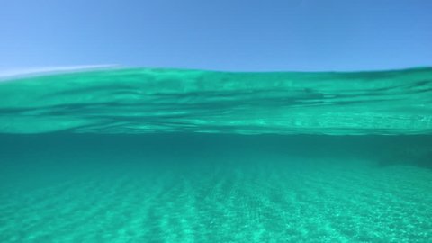 SLOW MOTION, HALF UNDERWATER: Picturesque view from the turquoise ocean of the distant island in the sunny Mediterranean. Cinematic half half of crystal clear sea and stunning Sardinia on a sunny day.