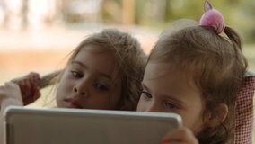 two small cute sisters hold a tablet and watch a cartoon on it
