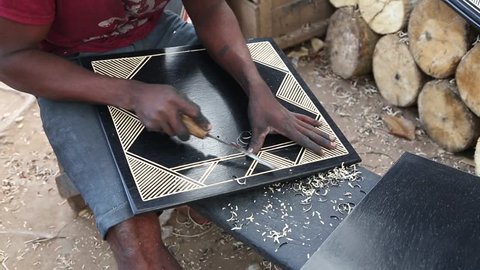 African Artifacts. A man makes patterns on polished wooden boards in a market.