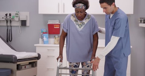 Young male nurse helps senior black woman walk with crutches. Middle aged African woman at rehab center supporting herself on crutches while receiving help from RN