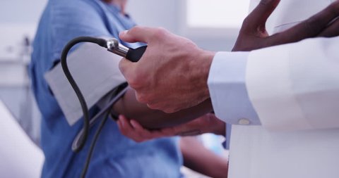 Close-up of young doctor pumping blood pressure gauge to measure black womans vitals. Tight shot of young MD checking senior womans blood pressure with stethoscope