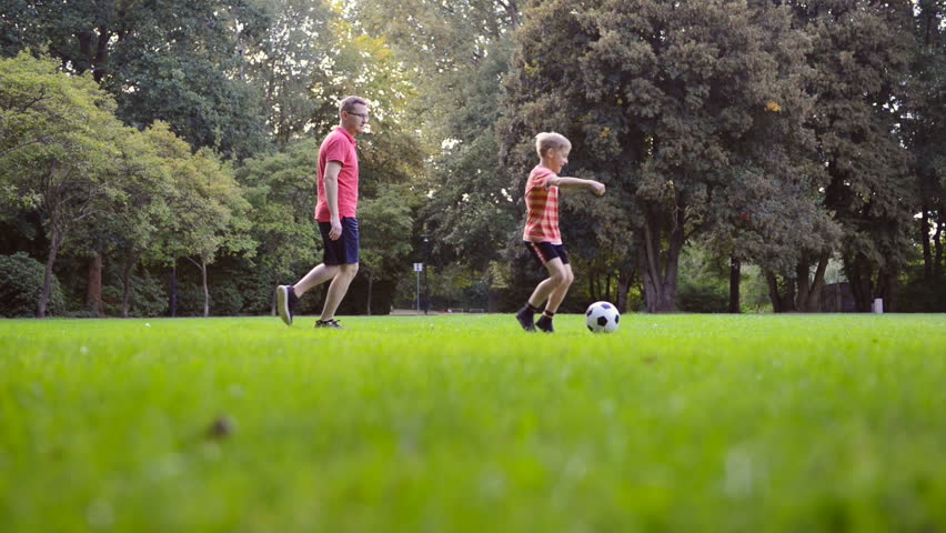 Happy child son  playing football with his father in park on green grass