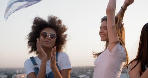 Three young female friends having a summer rooftop party, dancing to music with white shawl closeup 4k
