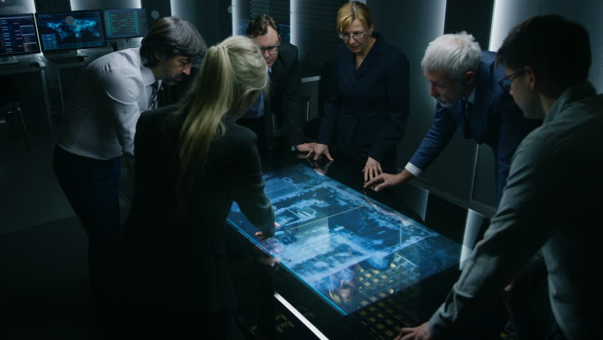 Team of Government Intelligence / FBI Agents Standing Around Digital Touch Screen Table and Tracking Suspect Vehicle Using Satellite Surveillance in the Monitoring Room. Shot on RED EPIC-W 8K Camera.