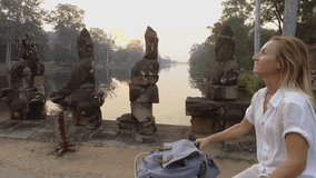 Slow motion of young woman cycling in Cambodia on ancient bridge in the Angkor Wat old temples complex. People travel adventure fun concept of tourist female riding bicycle in Asia 