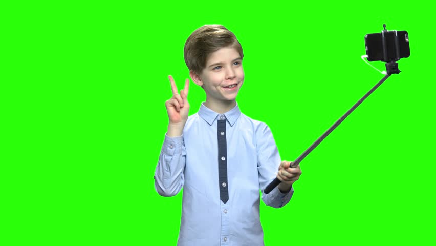 Smiling boy making photos using selfie stick. Making funny face, fooling around, victory gesture. Green hromakey background for keying. Royalty-Free Stock Footage #1016074261
