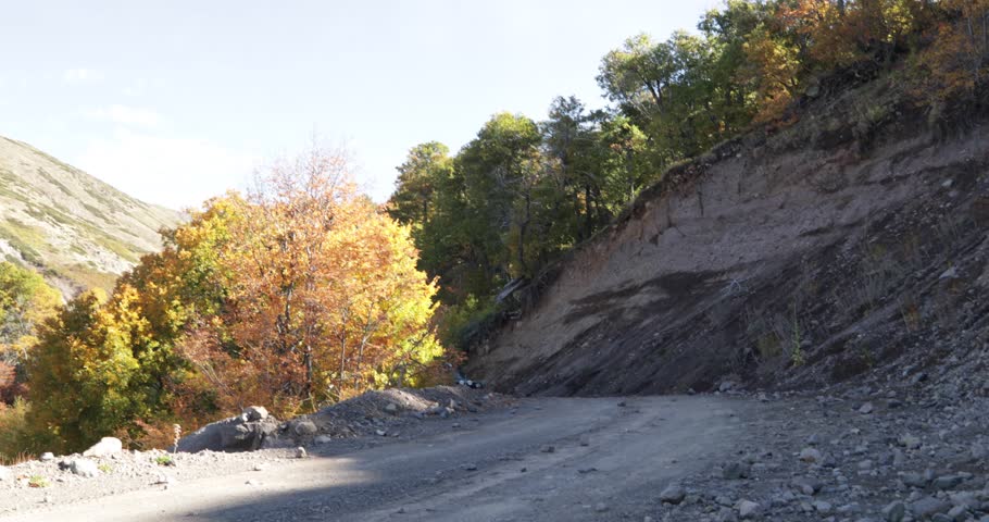 Van with trailer passing by a gravel road. Autumn, Nothofagus woods in Epu Lauquen Lagoons surroundings. Camera stays still while motorhome passes by road. Patagonia, Neuquen, Argentina