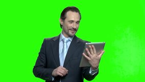 Successful businessman with tablet talking. Man talking on tablet computer having video chat with his kids and wife. Green hromakey background for keying.