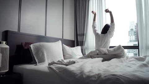Woman waking up in white bed in bedroom