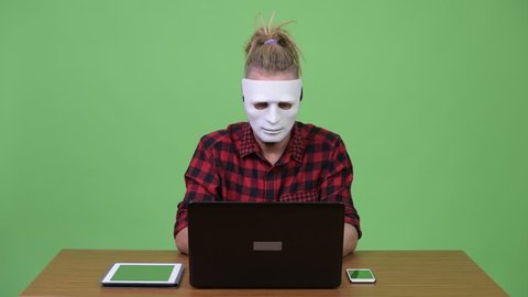 Hipster man wearing mask as hacker against wooden table