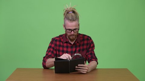 Handsome bearded hipster man reading book with magnifying glass against wooden table