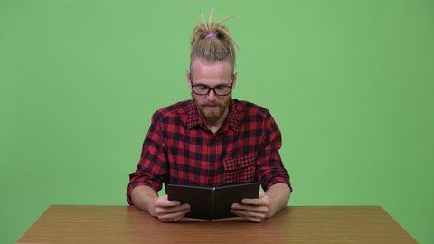 Handsome bearded hipster man reading book against wooden table