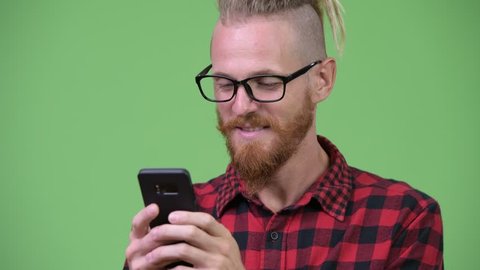 Happy handsome bearded hipster man with dreadlocks smiling while using phone