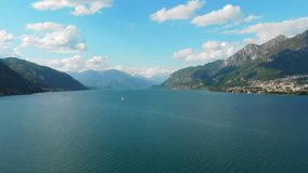 Scenic 4K drone footage above Lake Como in Italy. Nice white clouds in the blue sky and a sailboat on the lake add to the beautiful view.