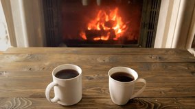 Closeup 4k video of couple taking mugs with hot tea from wooden table next tto burning fireplace