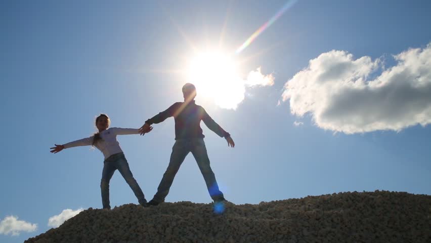Girl and boy in jeans stand and hold hands on stone pile at sunny day. sun in frame