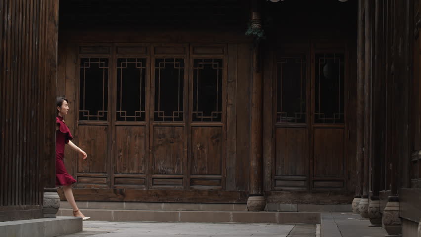 Pretty young Chinese woman in red dress walking in the Chinese style street in slow motion