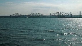 A slow-motion video of the view from a boat, of the three bridges in Edinburgh, on a sunny day.