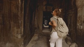 Young woman contemplating ancient temple, travel discovery adventure concept in tropical vacations; blond hair tourist female visiting old ruins Angkor Wat, Cambodia