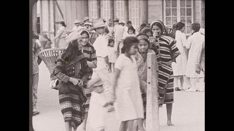1930s: Philippines: flappers carry baskets through market streets. Girls of Baguio smoke stogies.