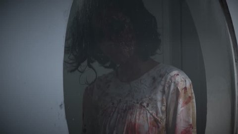 Scary ghost girl with bloody clothes in the mirror at dark night. Halloween concept. Shot in 4k resolution