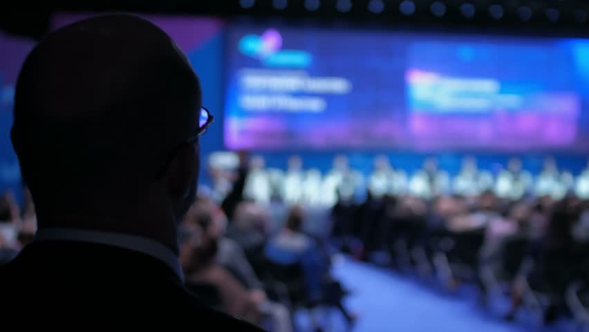 Businessman in a conference hall is looking at speakers presentation on the stage. Business meeting concept. Royalty-Free Stock Footage #1016122912