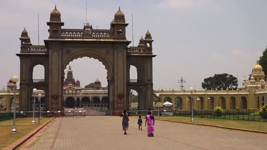 A wide view showing a family walking towards a beautiful Indian building. A static view as the family approaches an archway before the building