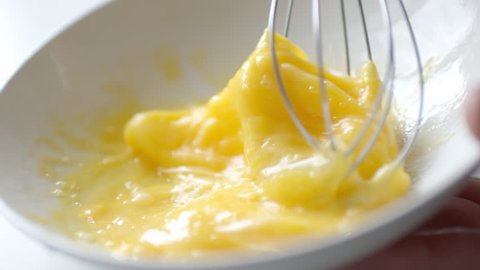 Slow motion crop shot of woman preparing homemade omelette mixing with whisk eggs.