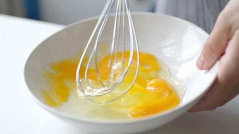 Slow motion crop shot of woman preparing homemade omelette mixing with whisk eggs.
