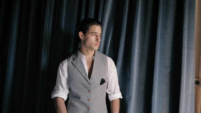 Attractive young fashion man in a suit posing on a background of blue curtains. Slow motion
