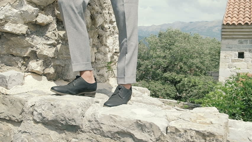 Attractive young fashion man in a suit walks around the old town along the plants. Slow motion
