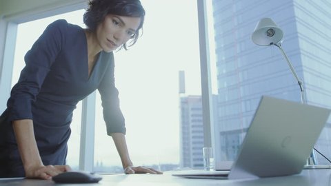 Low Angle Shot of Confident Businesswoman Leans on Her Office Desk, Writes Down Information in Documents and Looks at Laptop. Successful Woman Doing Business. Shot on RED EPIC-W 8K Helium Camera.