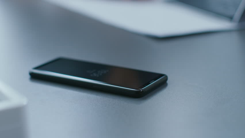 Out of Focus Shot of the Businesswoman Working at Her Office Desk Reaching Out for Her Smartphone and Starts Using It. Woman Picks up Mobile Phone from Her Desk. Focus on a Phone.Shot on RED EPIC-W 8K Royalty-Free Stock Footage #1016145775