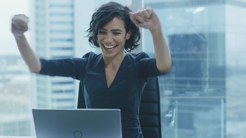 Beautiful Businesswoman Sitting at Her Office Desk, Raising Her Arms and Applauds in Celebration of a Successful Job Promotion. Shot on RED EPIC-W 8K Helium Cinema Camera.