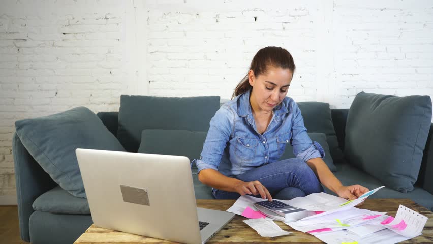 Happy attractive housewife woman accounting costs charges mortgage taxes and paying bills with laptop and calculator sitting on sofa in the living room in e-banking and home finances concept. | Shutterstock HD Video #1016148184