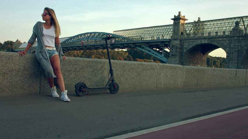Attractive woman with a scooter stands on the waterfront