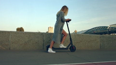 Attractive woman stands, scoots and rides on the electric kick scooter