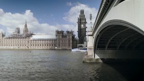 A 4k wide-shot along the Westminster Bridge and the river Thames in London, framing the Palace of Westminster and its iconic clocktower with Big Ben in spring/summer 2018 with a passing tourist boat.