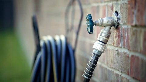 A hand turning off an outdoor water hose faucet with water dripping from the faucet.: film stockowy