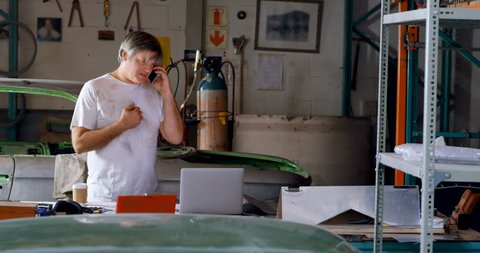 Male mechanic talking on mobile phone in garage 4k
