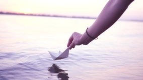 Man with a paper boat in water over beautiful sunset. Origami ship Sailing. Dreams, future, freedom or hope concept.