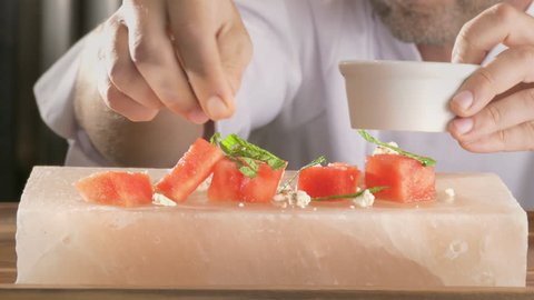 Chef preparing healthy gourmet food, watermelon and feta cheese with mint leaf garnish served on Himalayan salt block 