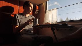 man is sitting in a Railway carriage train at the window of a compartment the car is drinking tea and coffee is talking. slow motion video. two men drinking tea on the train talking the train social