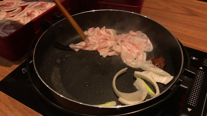 Preparing delicious thin slice of bacon and vegetable stir in hot pan. Japanese traditional food style called Sukiyaki. Selective focus.
