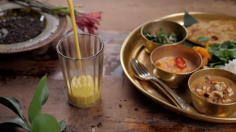 Beautiful and homemade fresh Indian sri lankian drink - mango lassi. On wooden table, garnished with fresh mint. Natural light, with carry traditional food rice