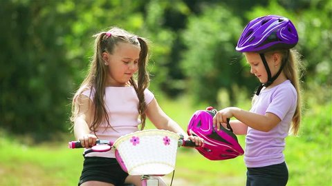 The older sister helps the younger girl to put on a safe helmet before riding a bike on a Sunny summer day in nature and give five to each other . Safety, sports, recreation